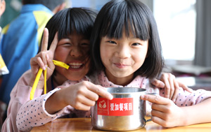 Two smiling Chinese school children eating lunch