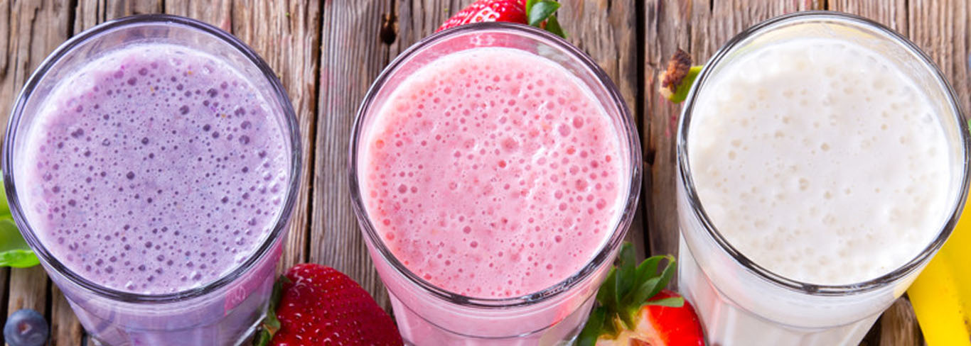 purple, pink and white smoothie on wooden table surrounded by berries